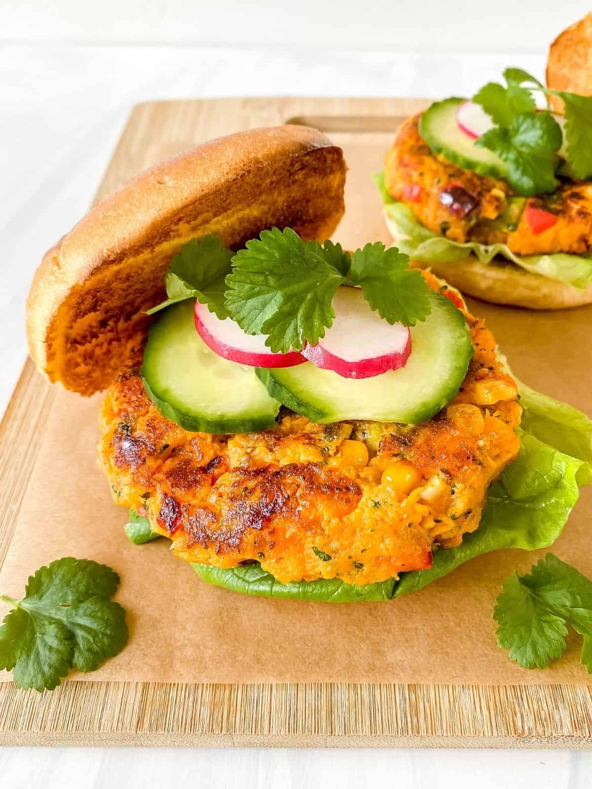 two sweet potato burgers in buns with salad on them on a wooden board.