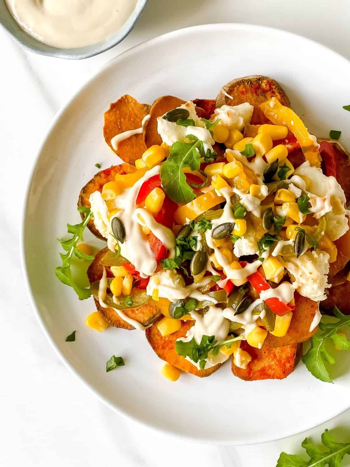 sweet potato nachos without beans on a white plate on a striped cloth next to a small bowl of tahini.