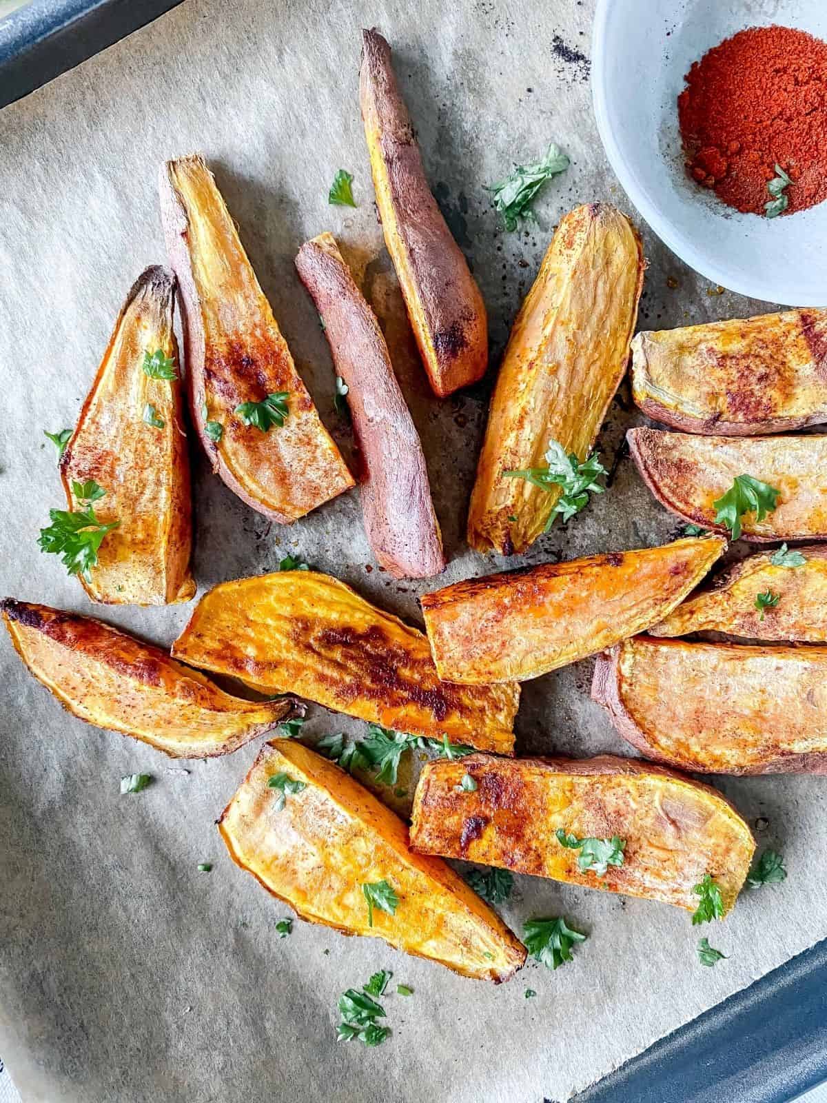 sweet potato wedges on a baking tray with a blue bowl of sweet paprika next to them.