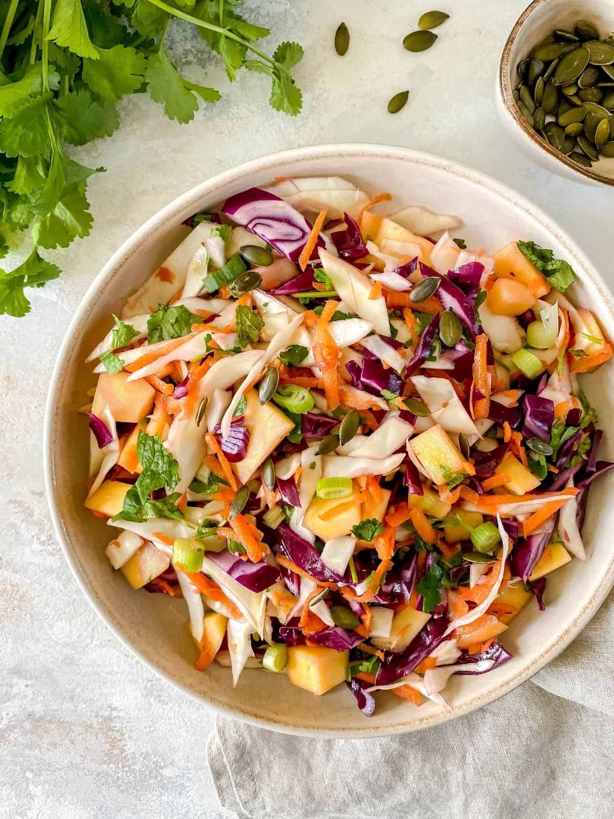tropical mango coleslaw in a brown bowl with fresh herbs next to it.