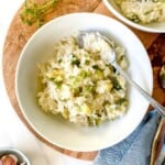 fennel risotto in a white bowl with a spoon in it on a wooden board.