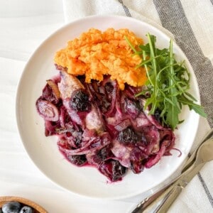 blueberry chicken with sweet potato mash and arugala on a white plate on a white and grey cloth.