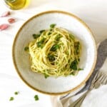 broccoli asparagus pasta in a bowl with a brown rim with forks on a white cloth next to it.