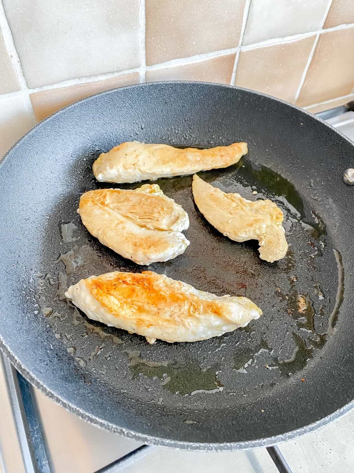 chicken frying in a black skillet on a stove top.