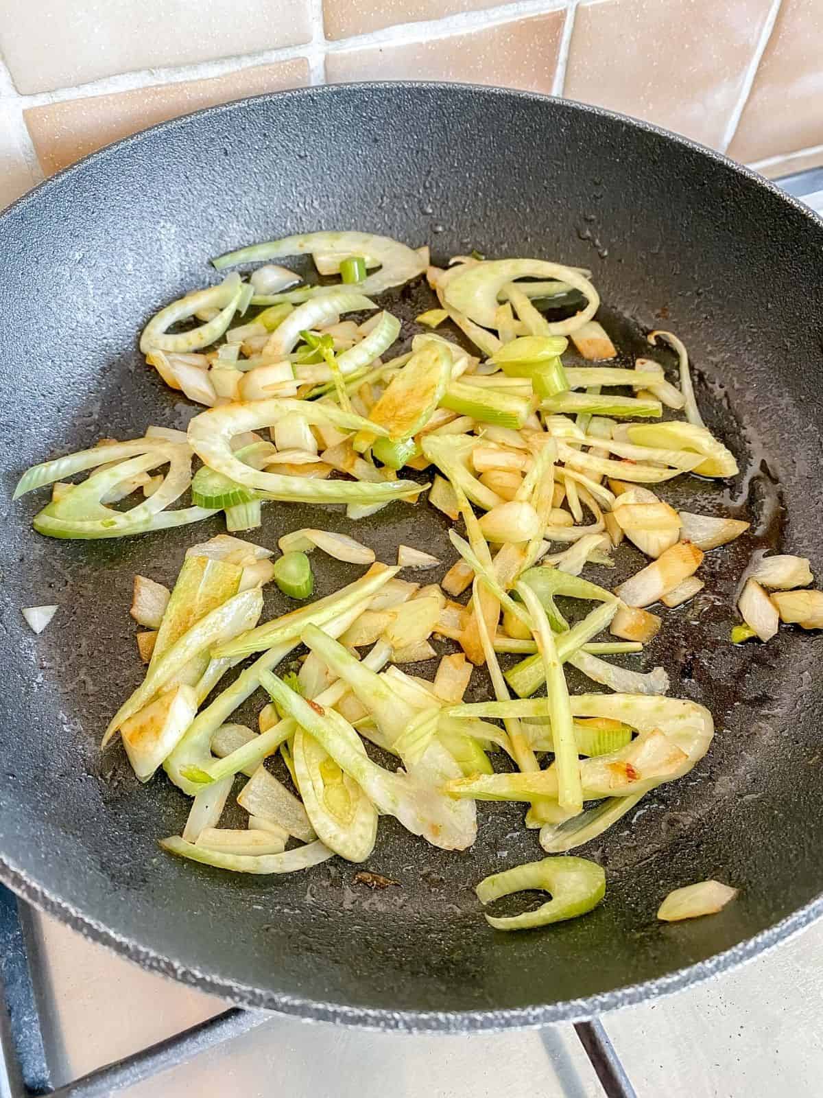 onion and fennel frying in a black skillet on a stove top.