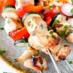 grilled turkey kabobs on a grey plate with slaw and radishes in the background.