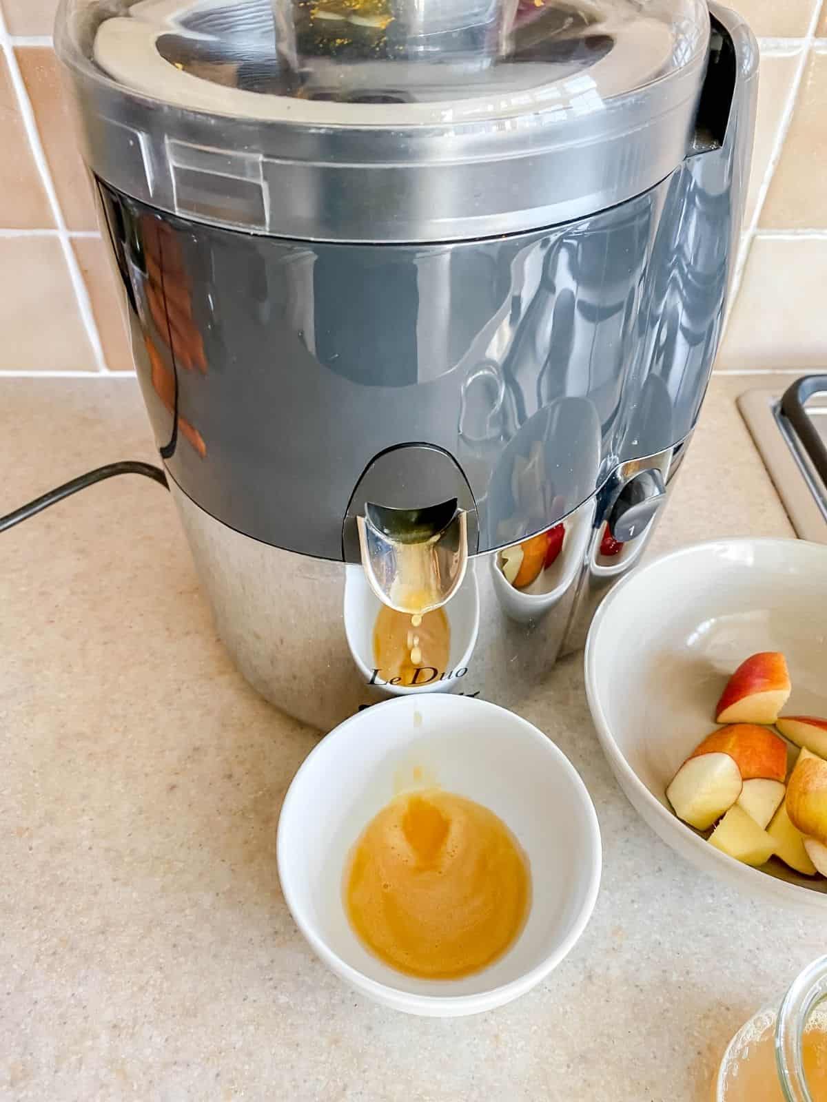 making apple ginger juice though a juicer next to a bowl of apple pieces.