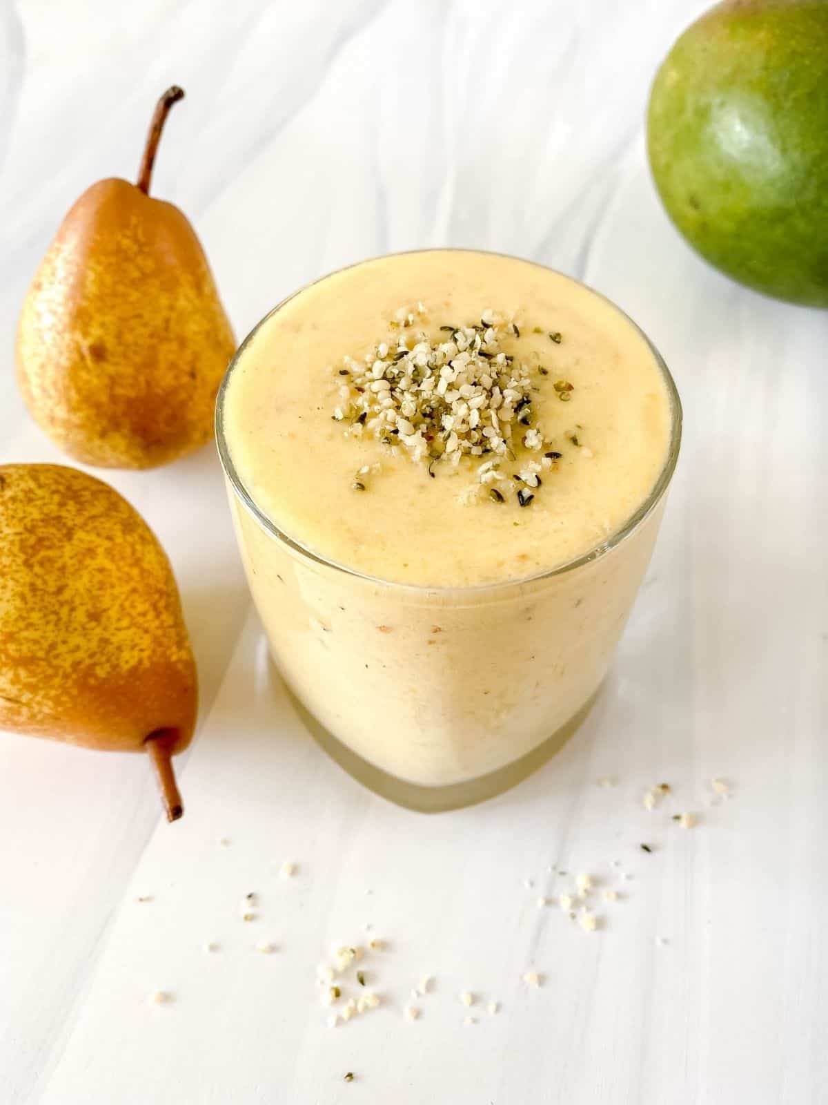 mango pear smoothie in a glass with hemp seed on top next to pears and a mango.