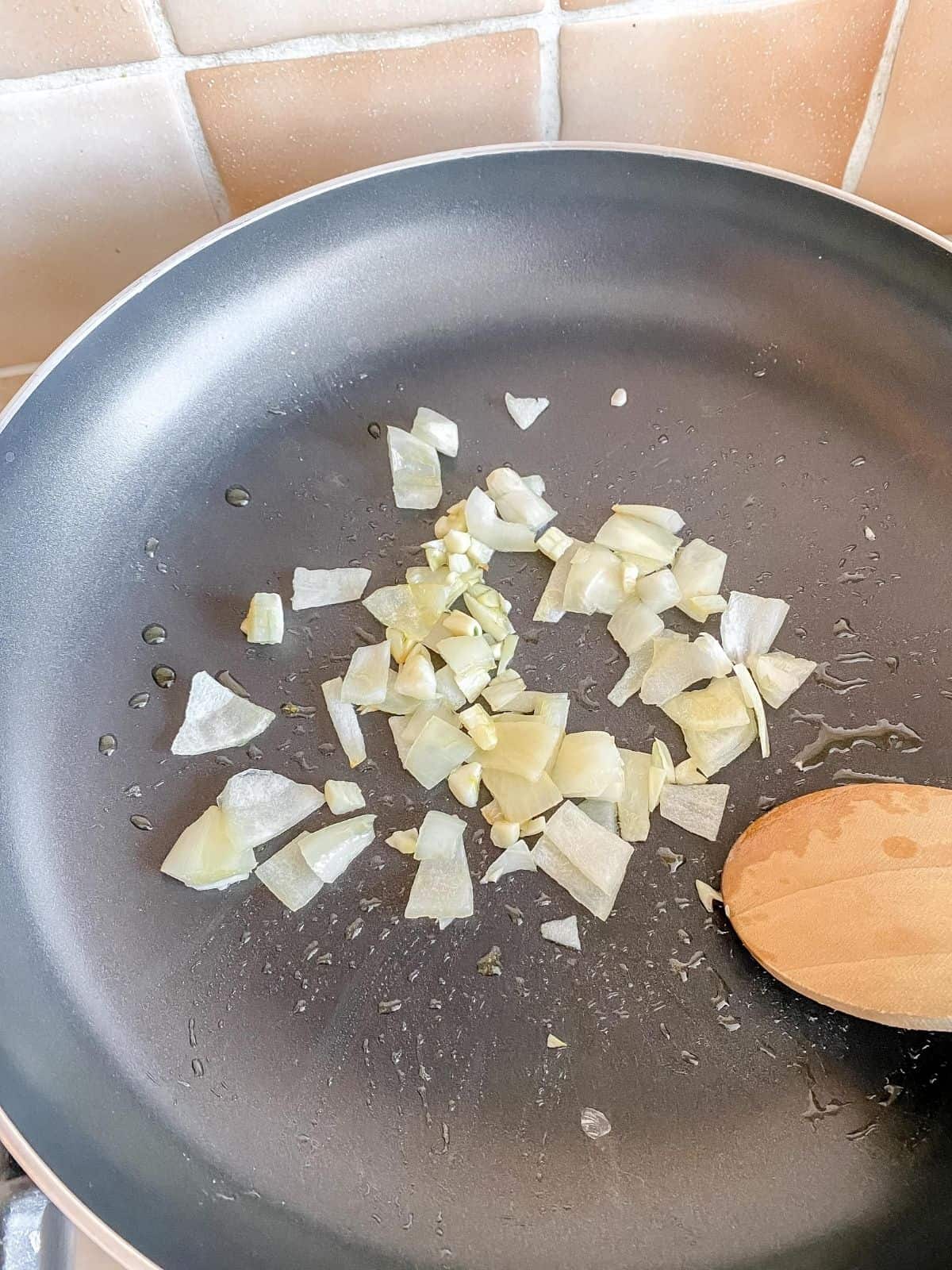 onion and garlic in a frying pan being stirred with a wooden spoon.