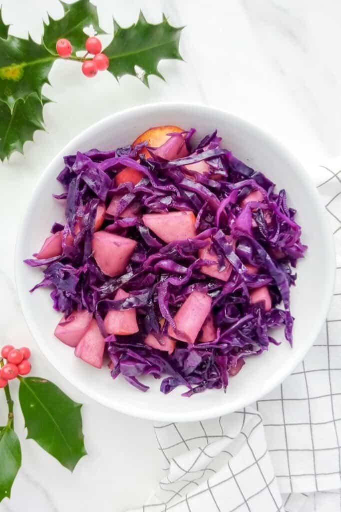 red cabbage with apples on a white plate with holly next to it.