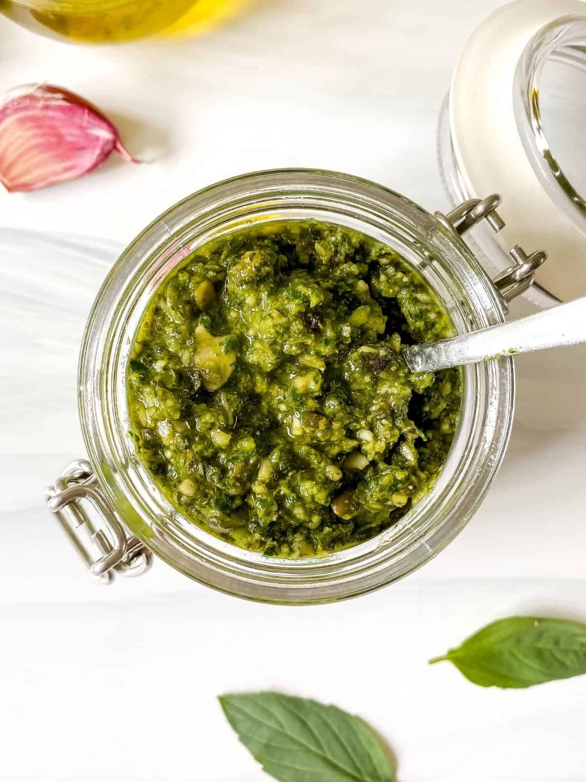 Thai basil pesto in a glass jar next to basil leaves and garlic.