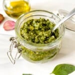Thai basil pesto in a glass jar with a bottle of olive oil and garlic cloves in the background.