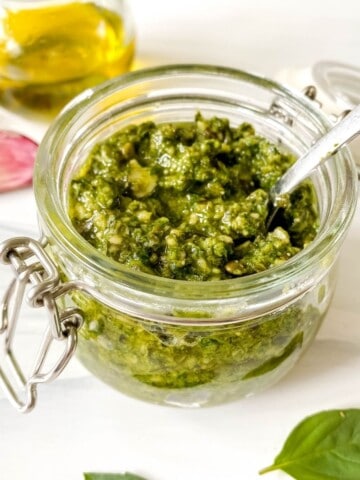 Thai basil pesto in a glass jar with a bottle of olive oil and garlic cloves in the background.