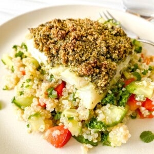 baked cod with pesto on tabbouleh on a cream plate with a fork on it.