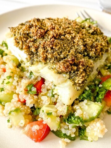 baked cod with pesto on tabbouleh on a cream plate with a fork on it.