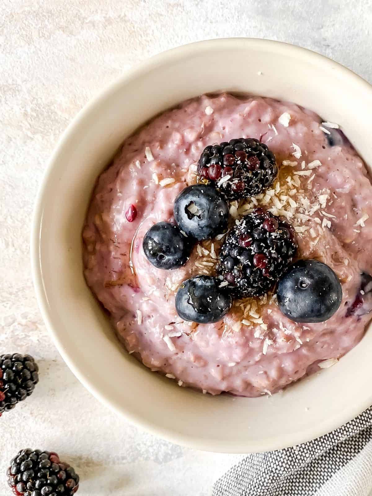 close up of berry porridge in a cream bowl next to fresh blackberries.