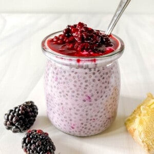 blackberry chia pudding in a glass jar with a spoon in it next to blackberries.