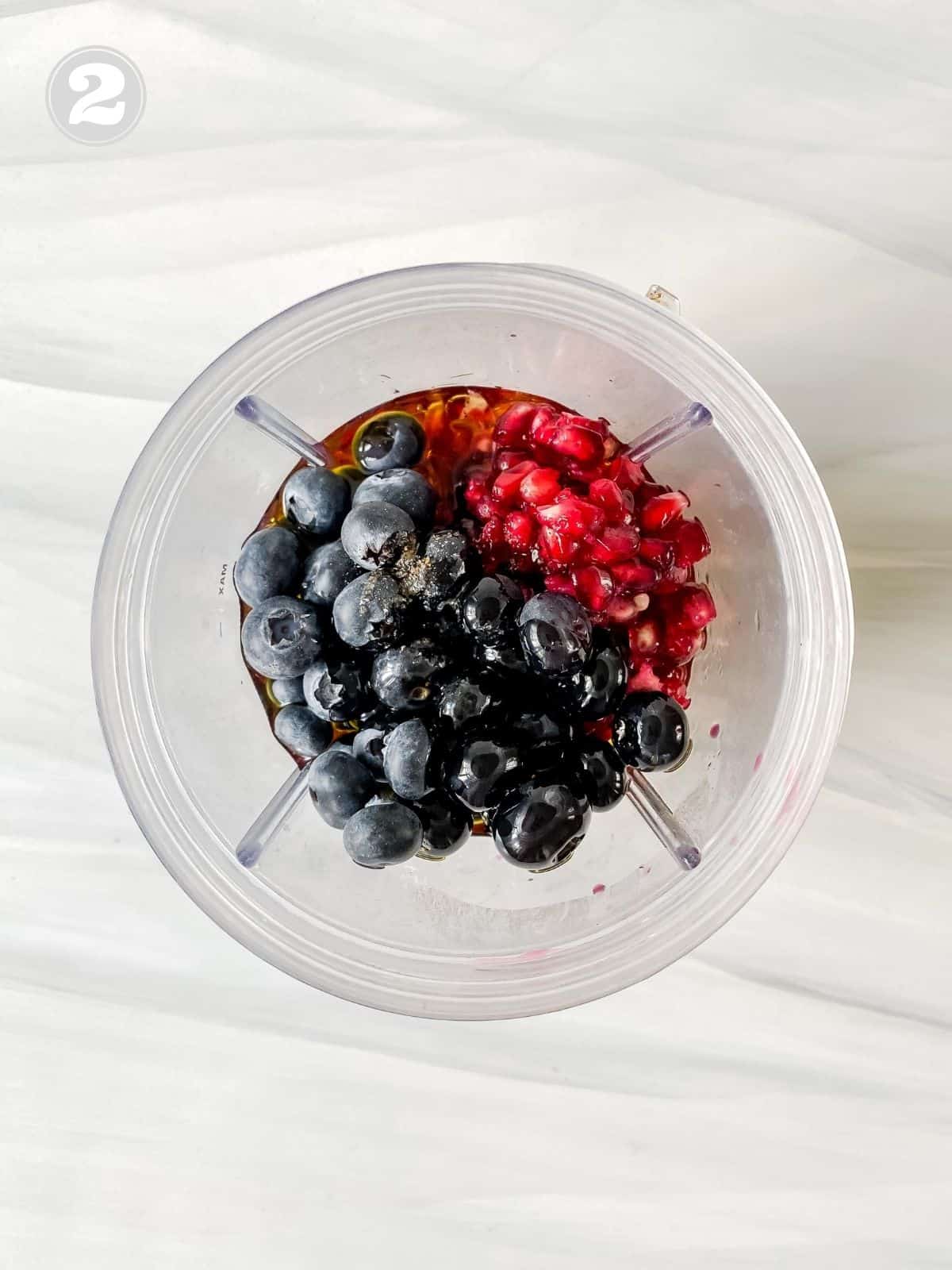 blueberries and pomegranate arils in a blender cup.
