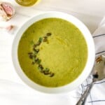 broccoli asparagus soup in a white bowl on a striped cloth with spoons.