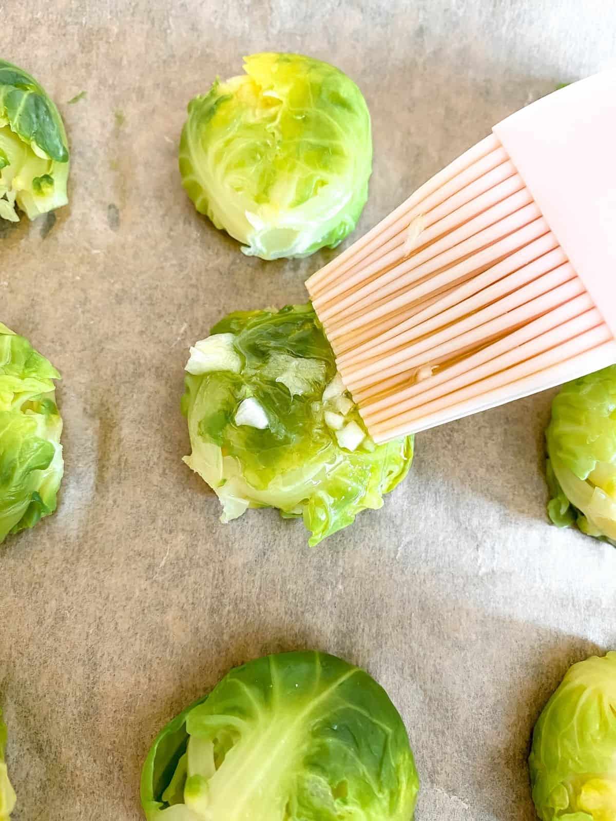brussels sprout being basted in dressing on a baking tray.