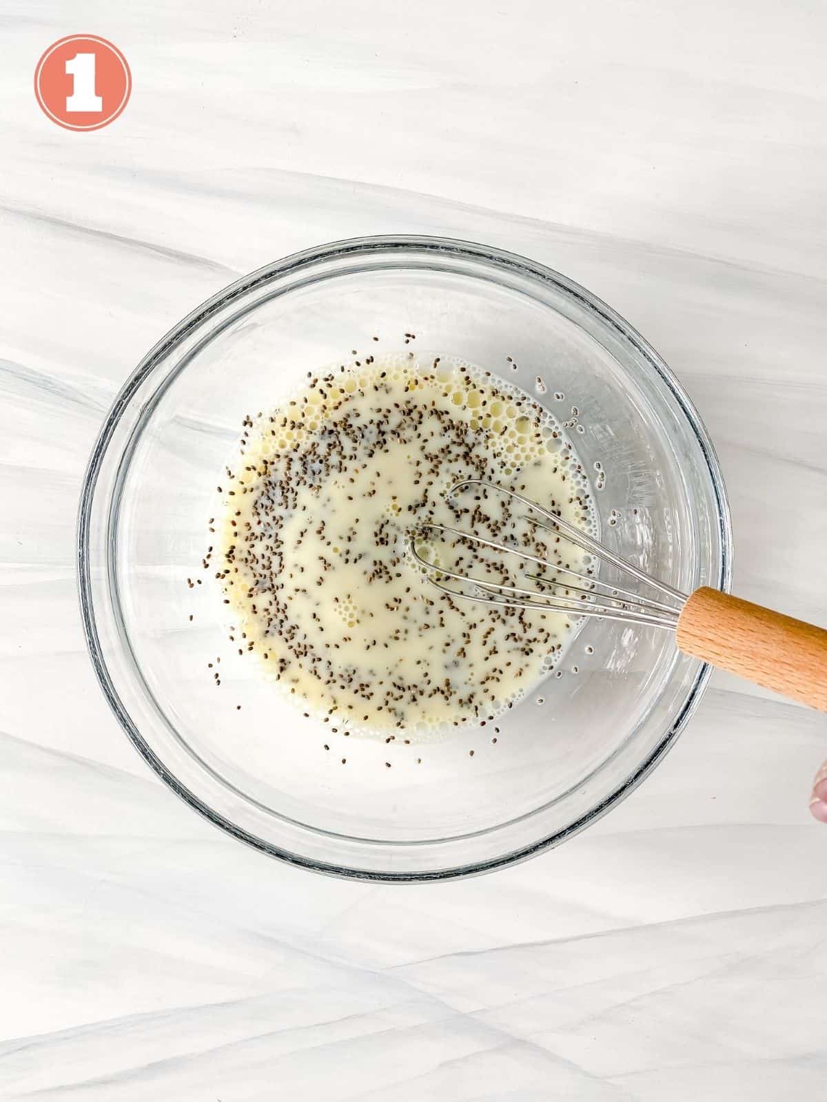 chia seeds and milk in a glass bowl being whisked.