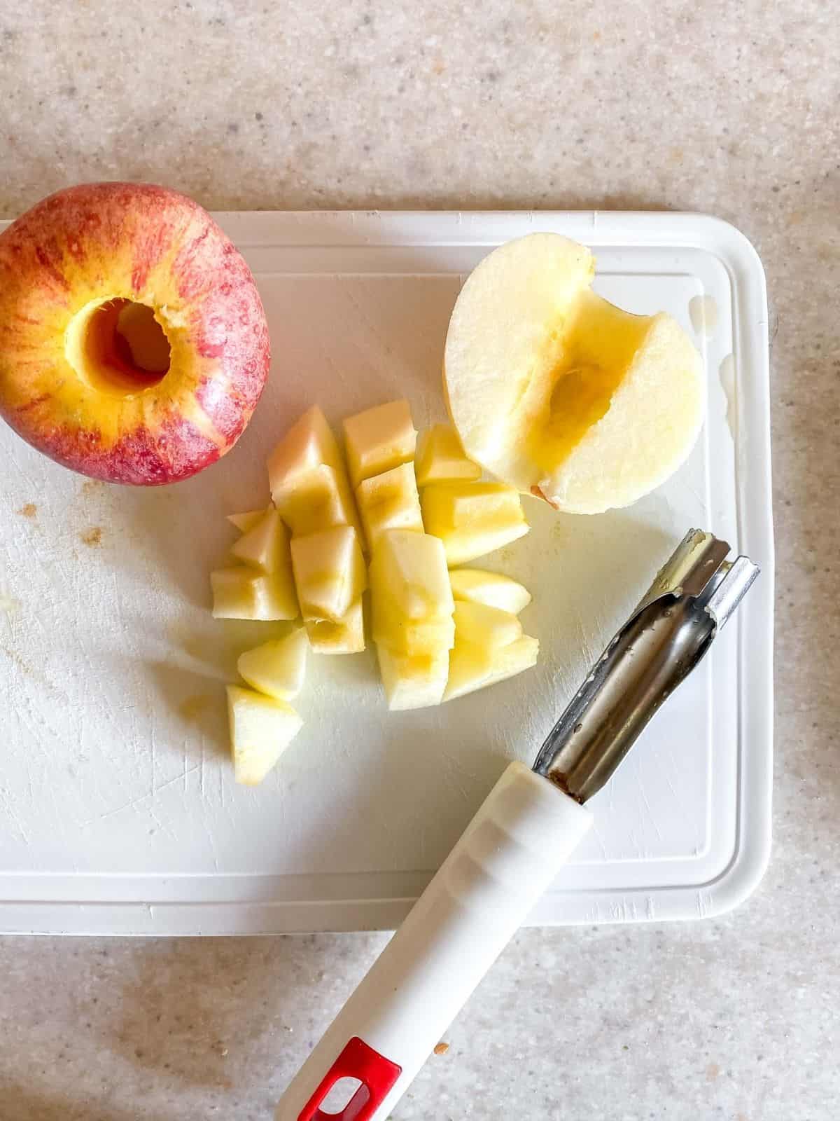 chopped apple on a white board next to an apple corer.