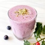 cranberry blueberry smoothie in a glass next to holly.