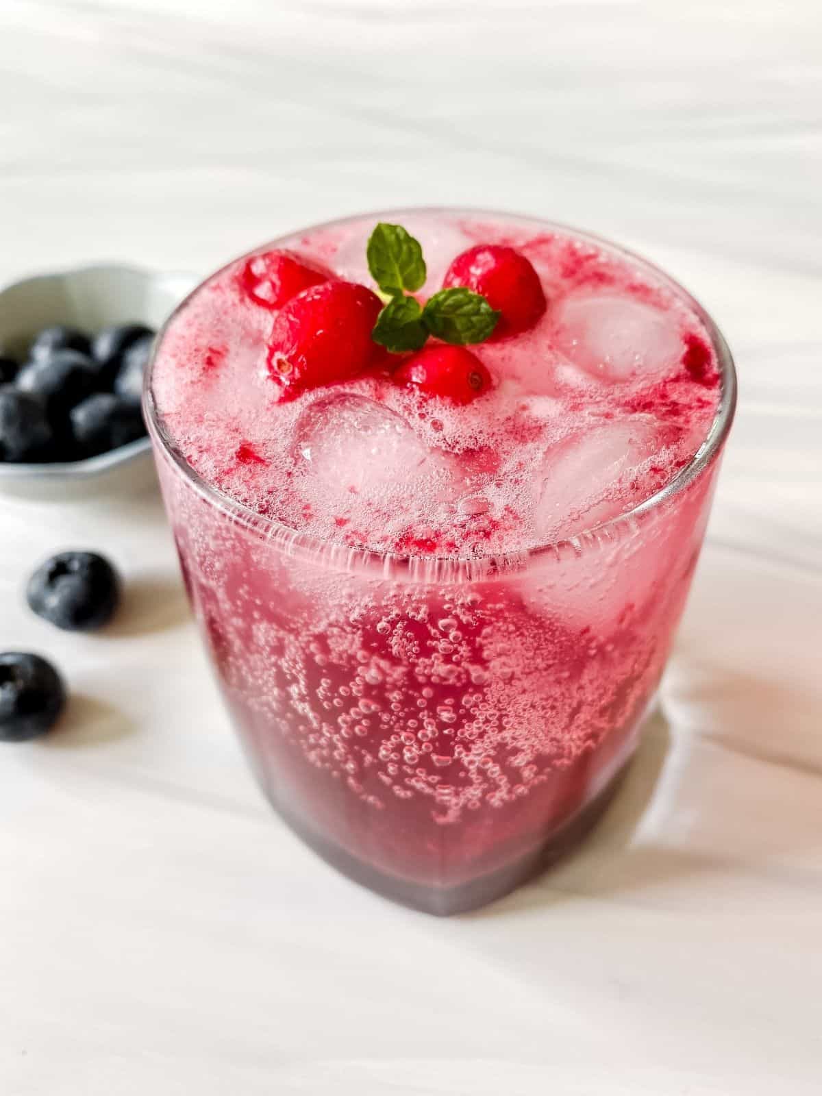 cranberry mocktail in a glass with blueberries in the background.