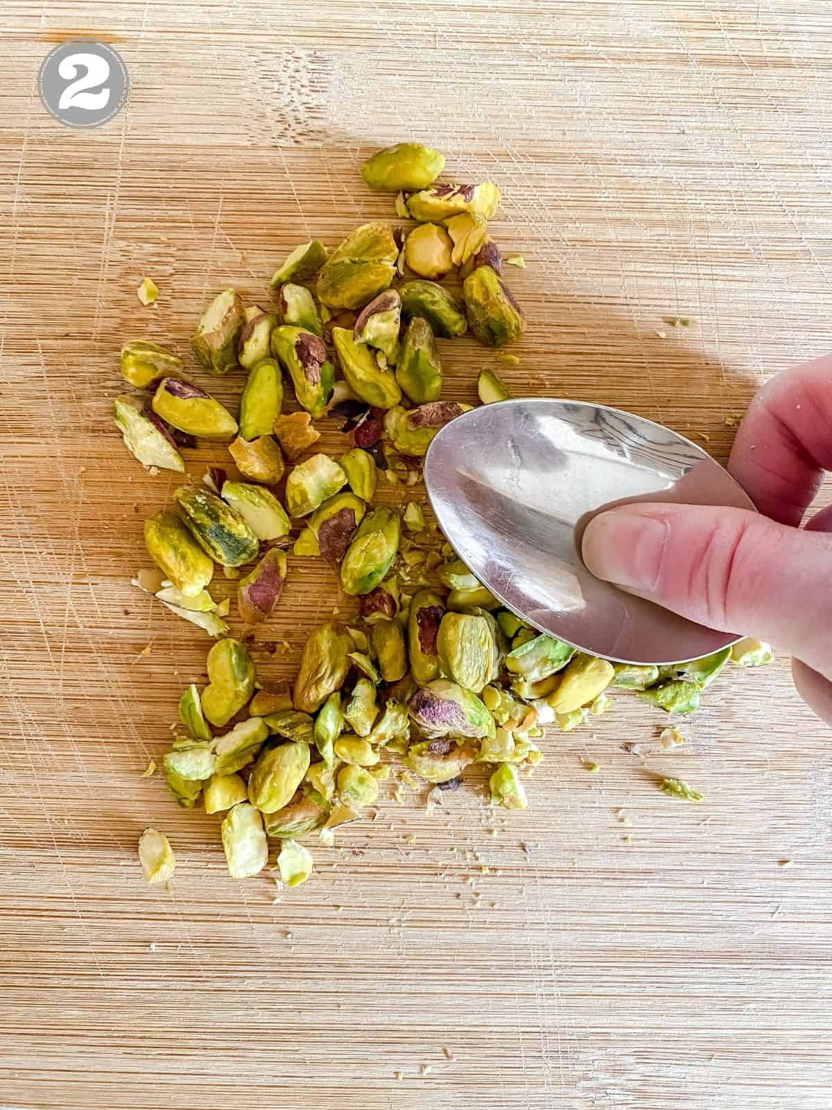 a spoon crushing pistachios on a wooden board.