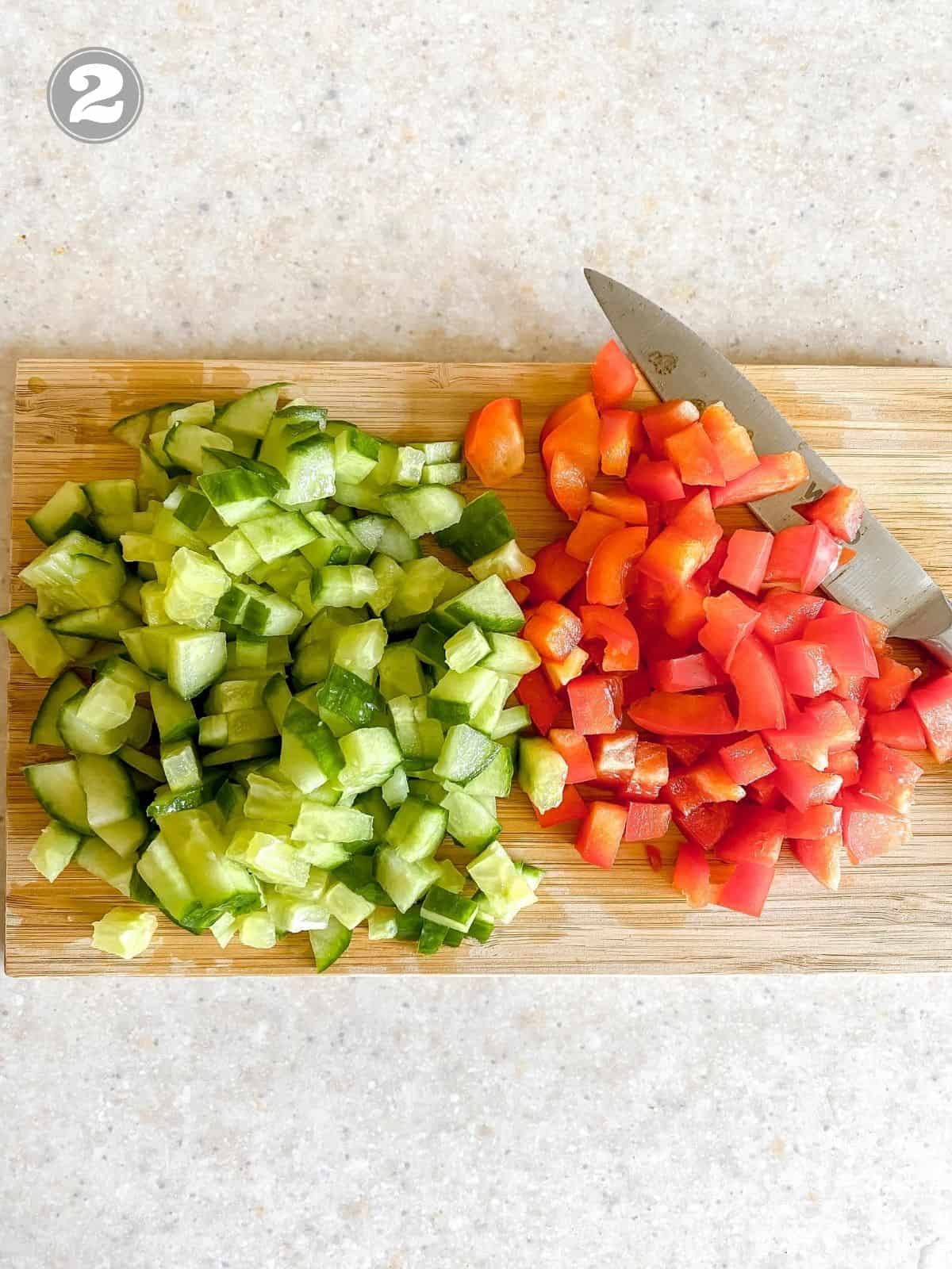 diced cucumber and bell pepper on a wooden board with a knife labelled number two.
