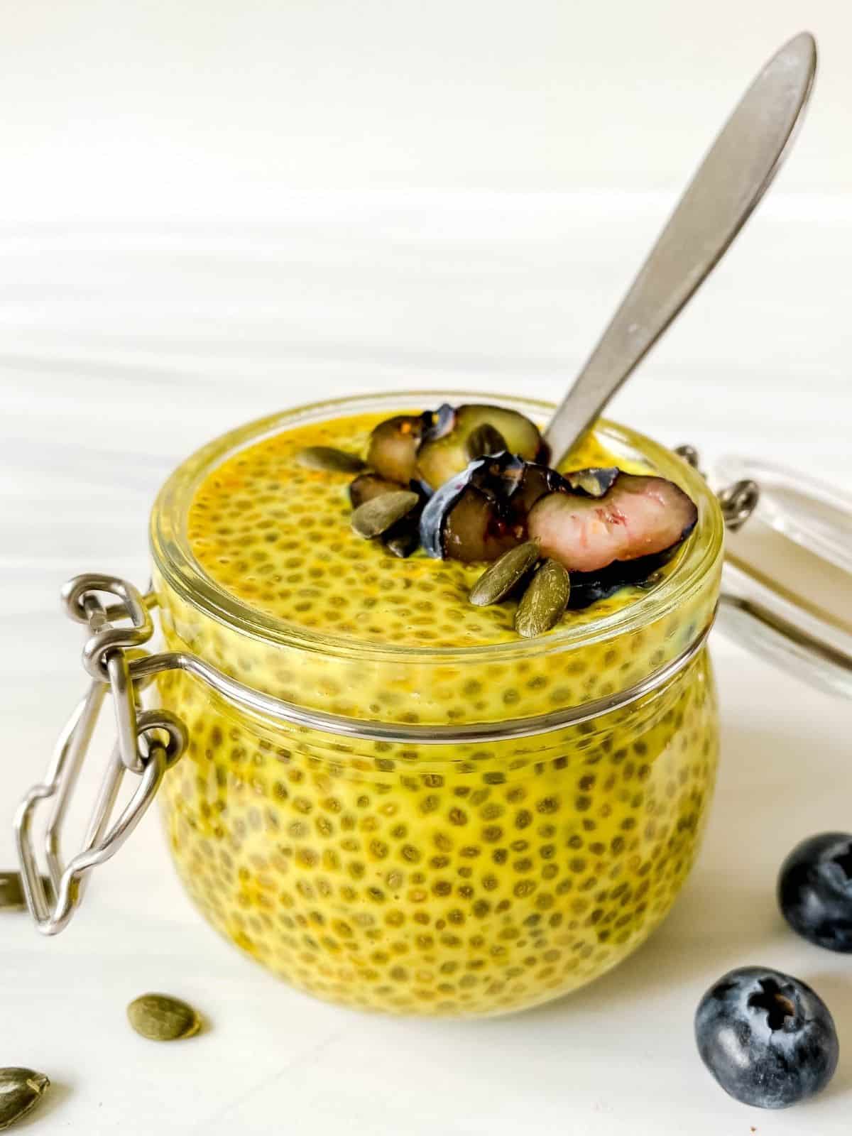 glass jar of golden milk chia pudding with blueberries on it and a spoon in the jar.