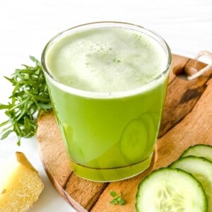 green juice in a glass on a wooden board with cucumber slices and ginger.