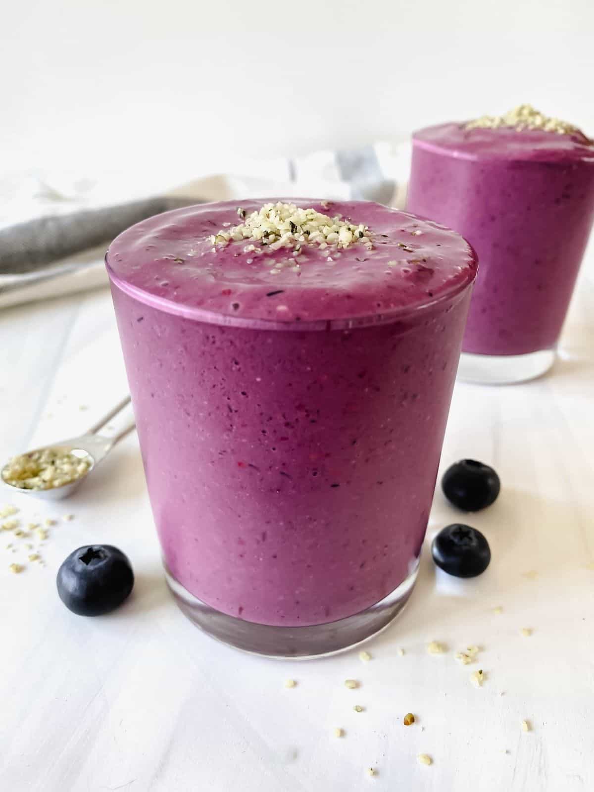 mixed blueberry blackberry smoothie in two glasses next to blueberries and a spoonful of hemp seeds.
