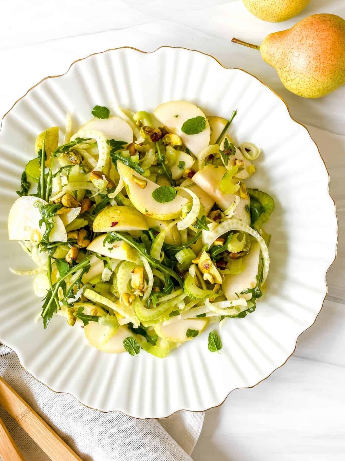 pear and fennel salad on a white plate with a gold rim next to pears. 