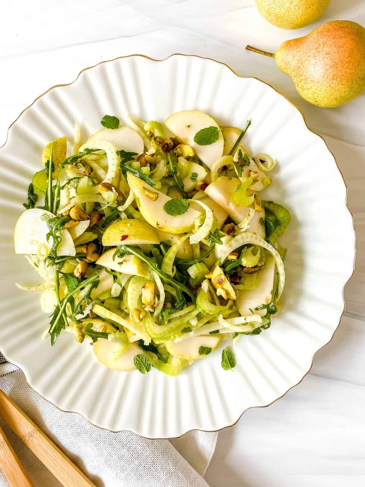 pear fennel salad on a white fluted plate next to pears.