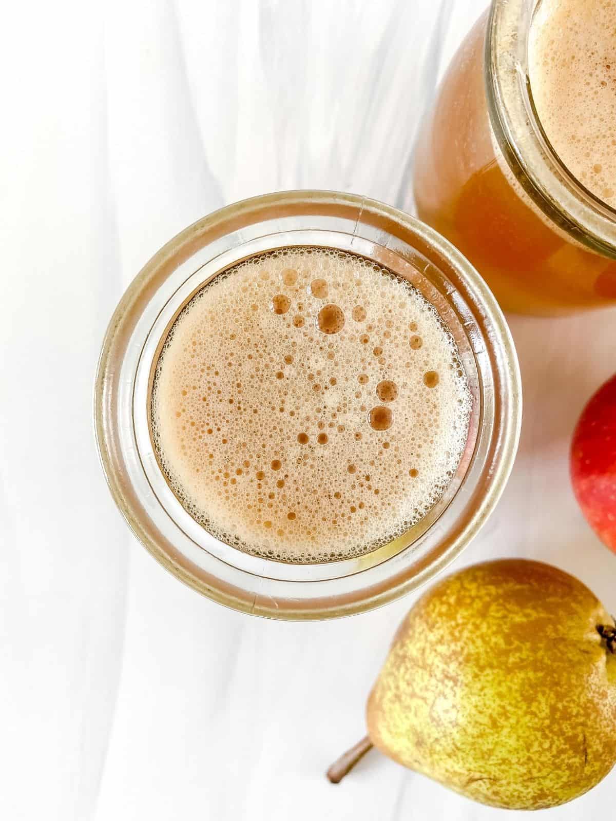 two glasses of pear apple juice next to a pear.