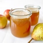 pear apple juice in two glass jars next to apples and a pear.