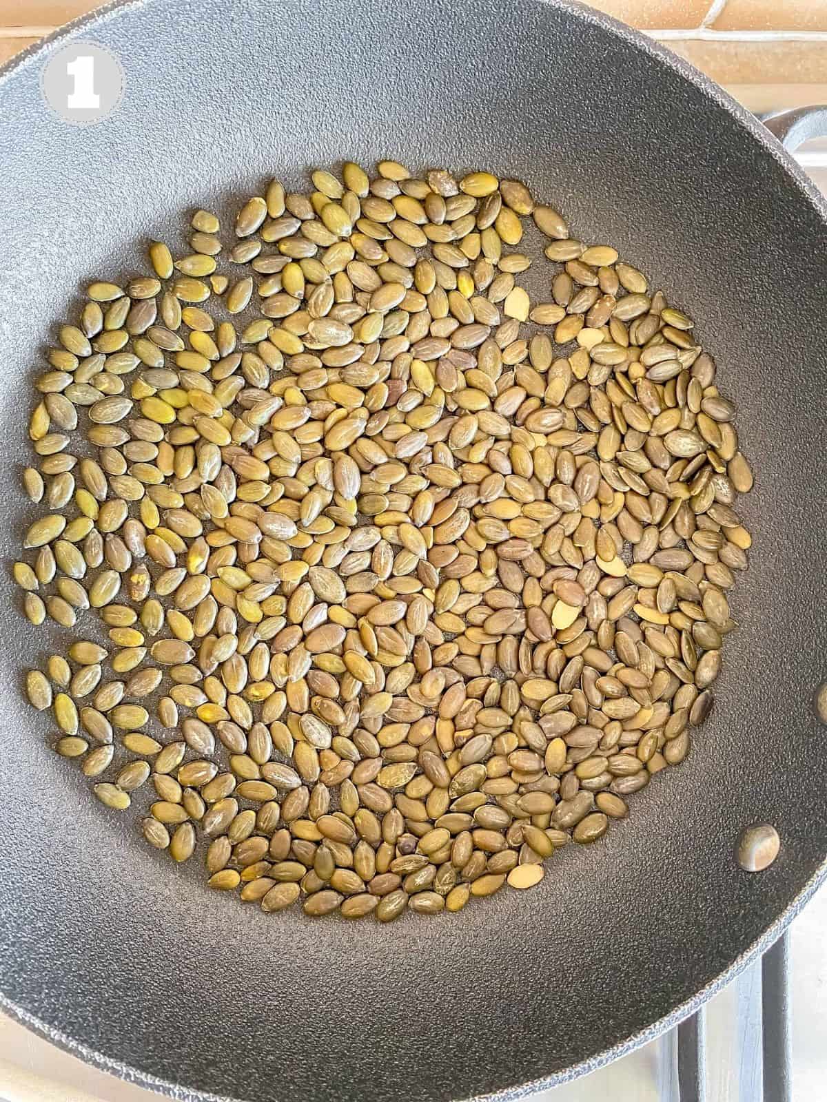 pumpkin seeds in a black frying pan.
