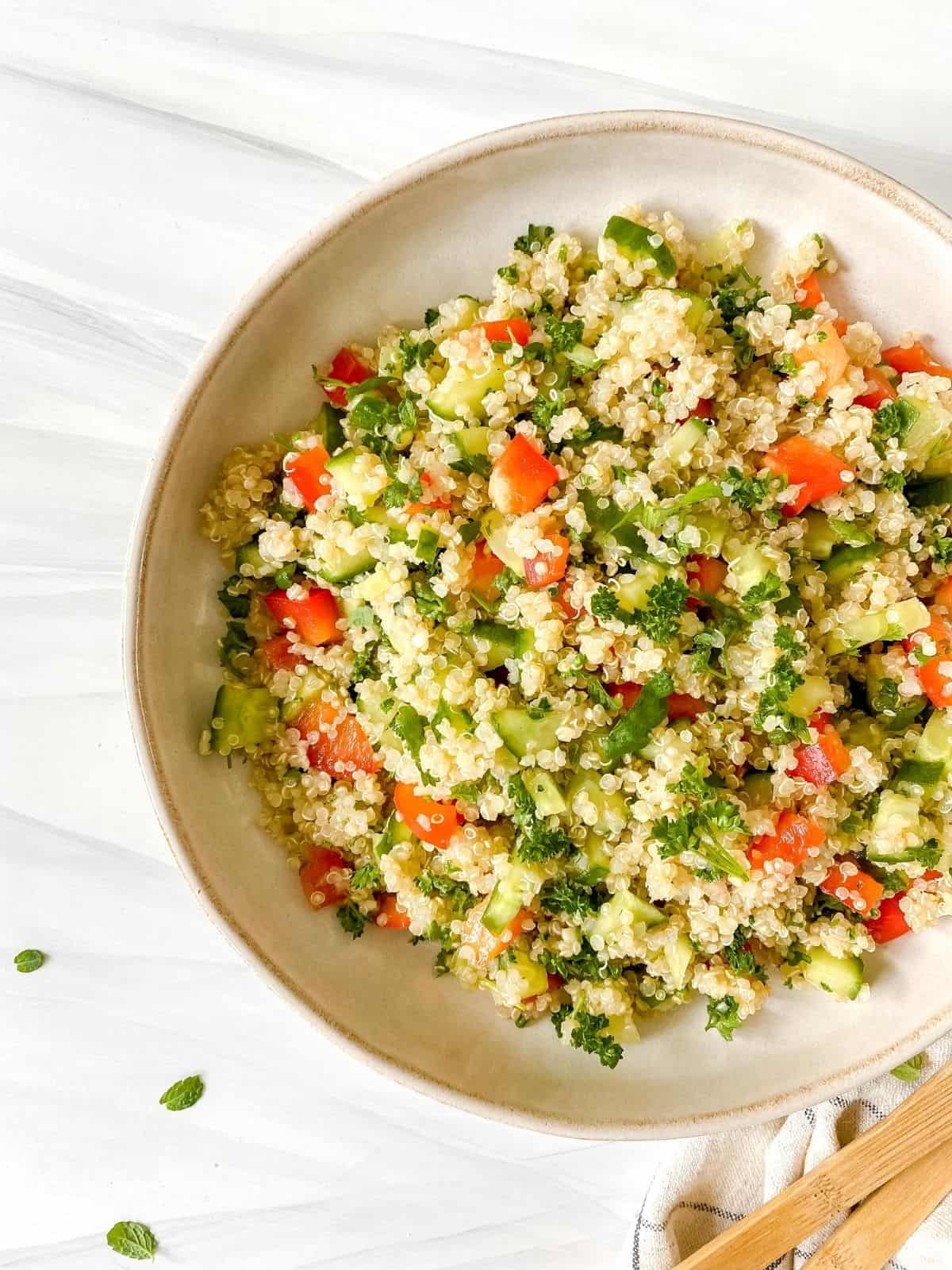 quinoa tabbouleh without tomatoes in a brown dish with herbs next to it.