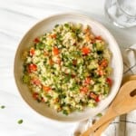 quinoa tabbouleh without tomatoes in a brown dish with wooden serving spoons next to it.