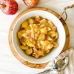 rhubarb and apple compote in a white bowl on a striped cloth with spoons.