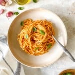 roasted red pepper ricotta pasta in a bowl with a fork in it next to olive oil and basil.