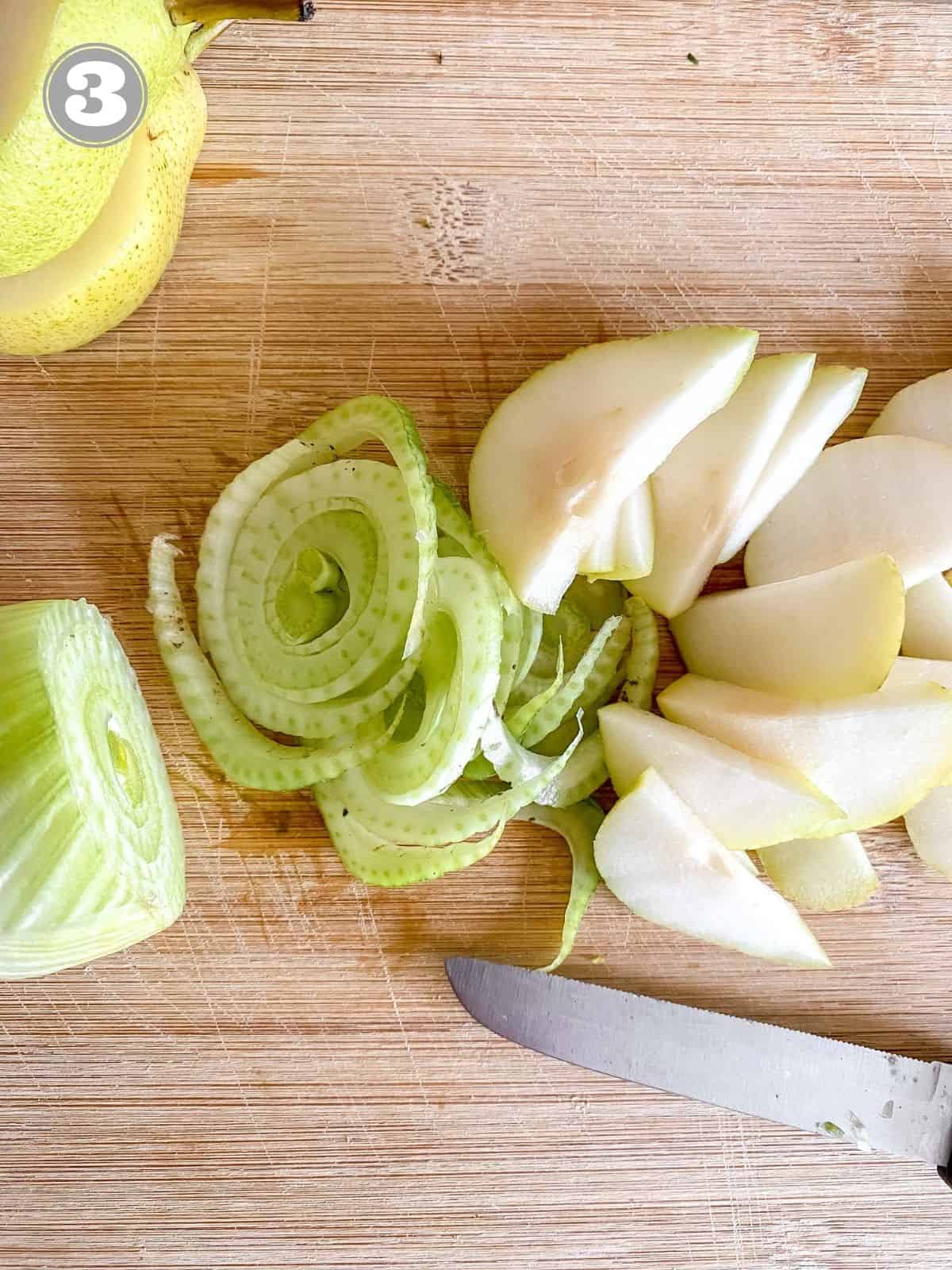 sliced pears and fennel on a wooden board with a knife.