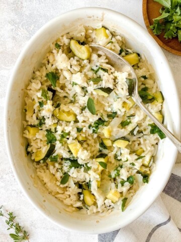 baked kale and zucchini risotto in a white pan with a spoon in it.