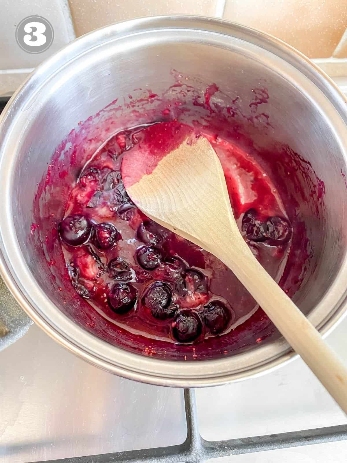 blueberries in a pot with a wooden spoon.
