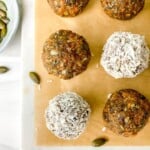carrot cake bliss balls on baking paper next to a bowl of pumpkin seeds.