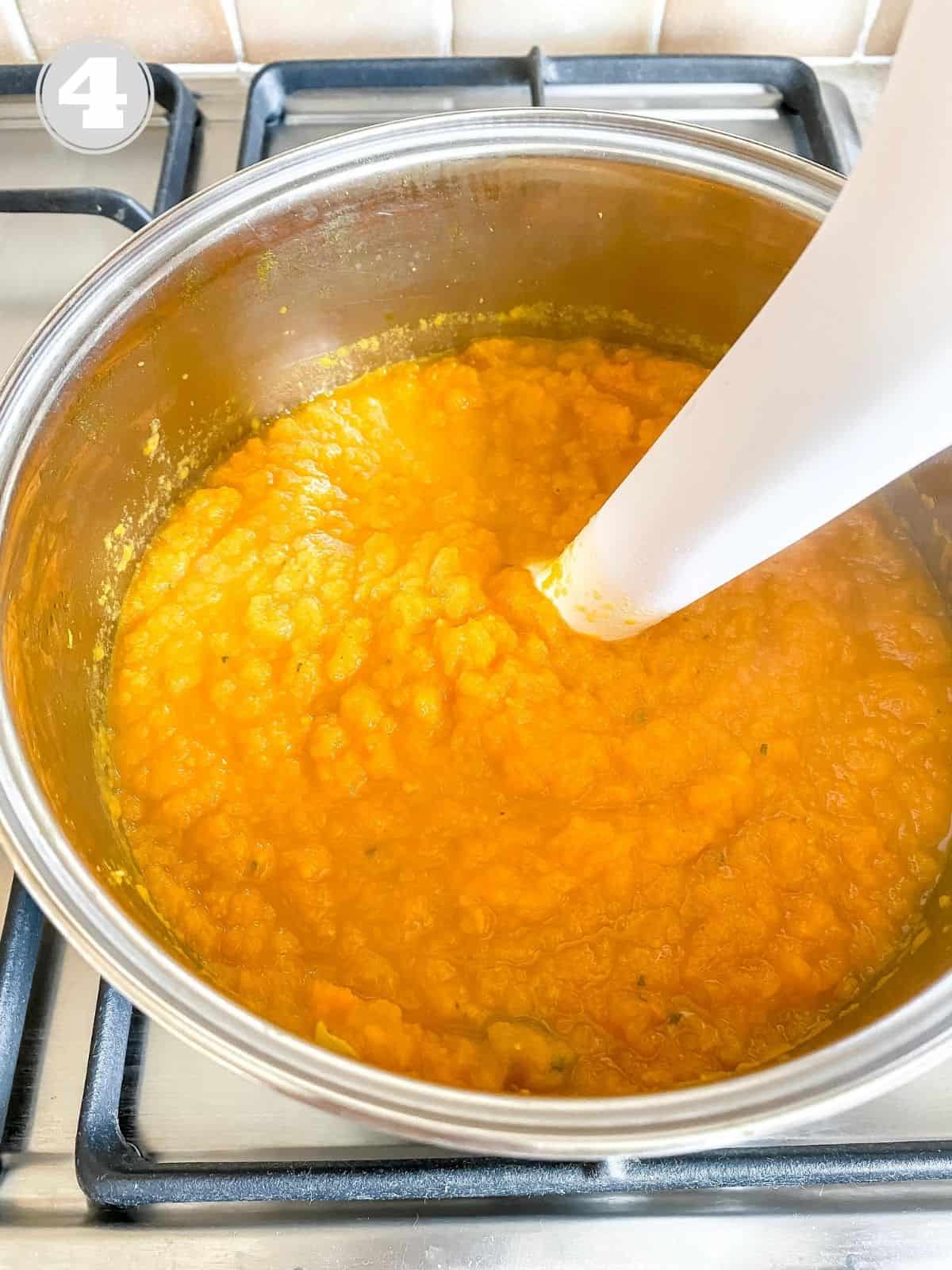 carrot soup being blended in a large pot.