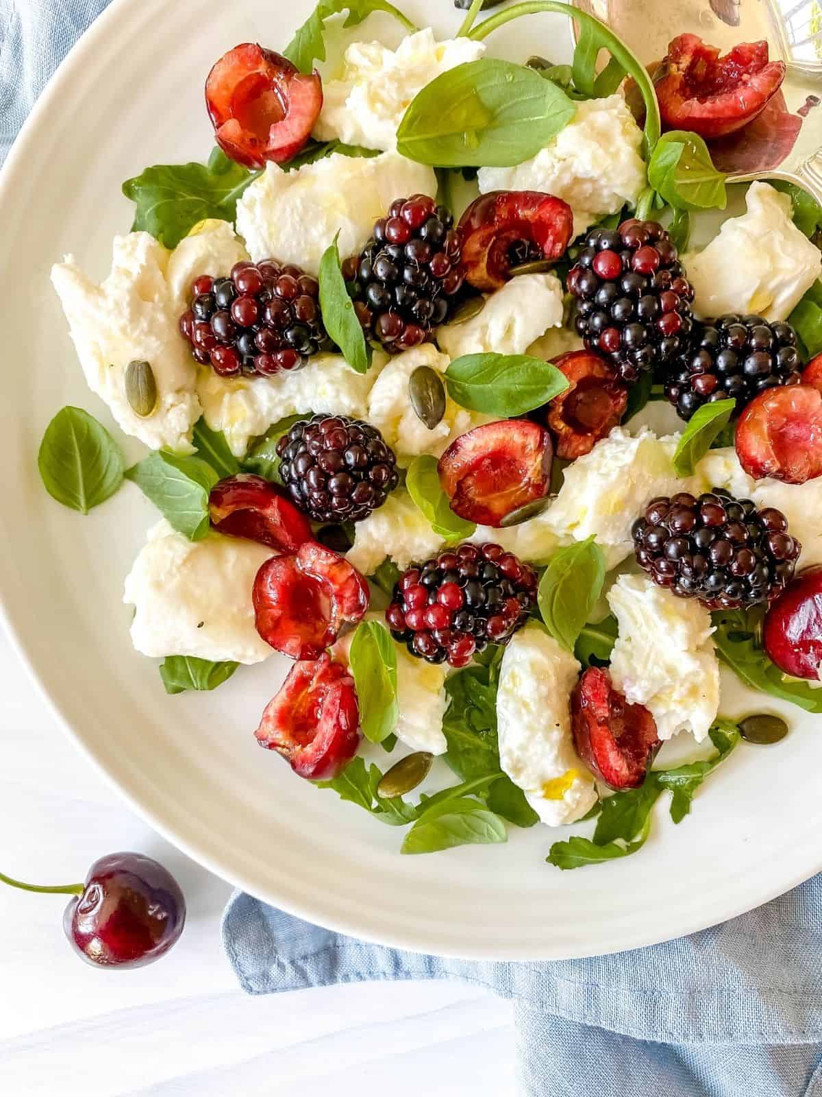 cherry caprese salad with blackberries on a white plate on a blue cloth.