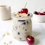 cherry overnight oats in a glass jar with a bowl of cherries in the background.