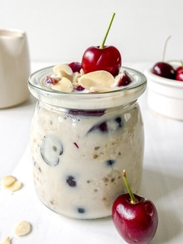 cherry overnight oats in a glass jar with a bowl of cherries in the background.
